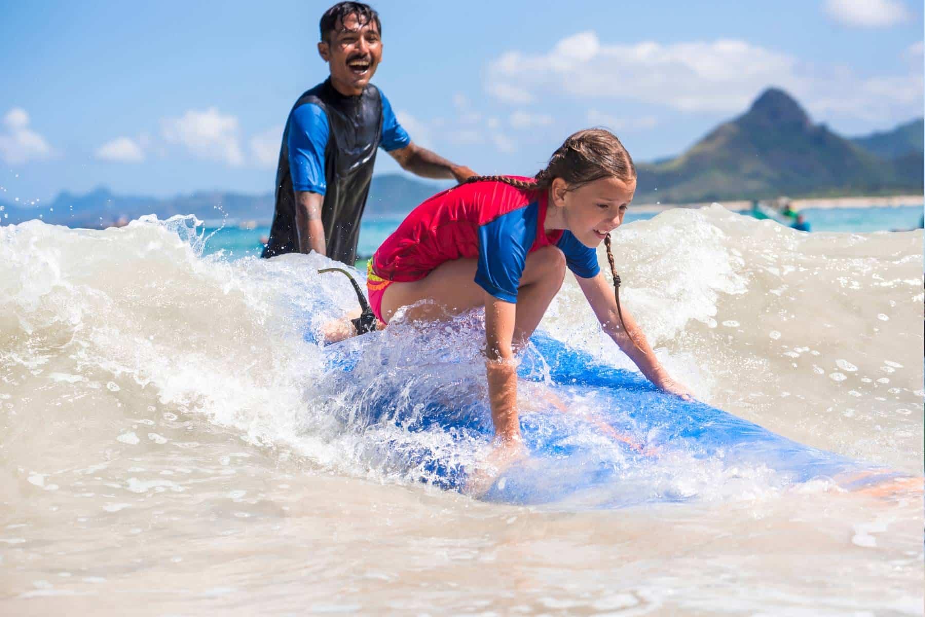 A girl rides her first wave while an instructor steadies the board behind her